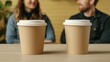 © Panisara - Closeup of coffee cups on a table, with two people in the background engaged in a relaxed conversation, enjoying a cozy coffee shop vibe