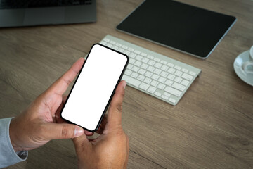 Poster - A smart person is using a laptop and smartphone at a modern office desk, holding a phone in one hand and typing on a keyboard, displaying digital communication and business with a white screen