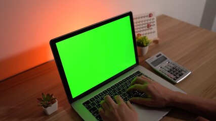 Laptop Workspace: Hands typing on a modern laptop with green screen, keyboard, and a neutral backdrop, showcasing a workspace setup for productivity and tech