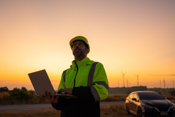 Fototapete - Engineer working on laptop in front of wind turbines for checking wind turbines of the field during beautiful sunset. Alternative energy concept.