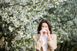 © anatoliy_gleb - Woman allergic suffering from seasonal allergy at spring in blossoming garden at springtime. Young woman sneezing and blowing nose with nasal handkerchief in front of blooming tree. Allergy concept.