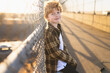 © Cavan Images - Young boy in flannel coat leans against fence on sidewalk