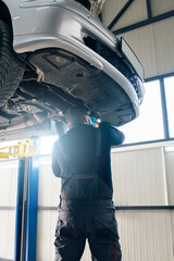 Fototapete - Serviceman checks car suspension on a column lift in car service