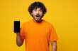 © ViDi Studio - Young shocked happy Indian man he wear orange t-shirt casual clothes hold in hand use mobile cell phone with blank screen workspace area isolated on plain yellow background studio. Lifestyle concept.