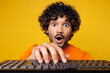© ViDi Studio - Close up young shocked surprised happy Indian man wear orange t-shirt casual clothes typing on pc computer keyboard look camera isolated on plain yellow background studio portrait. Lifestyle concept.