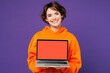 © ViDi Studio - Young smiling happy Caucasian IT woman she wear orange hoody casual clothes hold use work on laptop pc computer with blank screen workspace area isolated on plain purple background. Lifestyle concept.