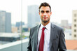 © Minerva Studio - Portrait of a young businessman posing on a rooftop with cityscape in background