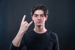 © vidiot - The young man showing rock and roll hand sign with his fingers isolated on black background. The focus is on the hand.