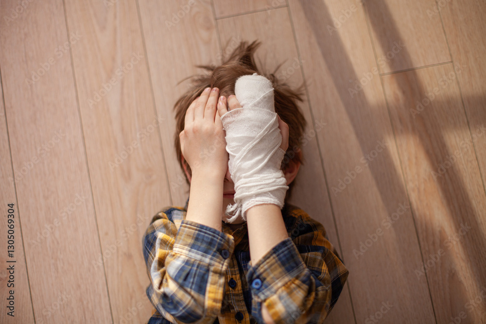 Child lying on floor covered his face with hands in gypsum cast. Boy ...