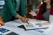 © amnaj - Professional women working together in corporate boardroom, pointing at financial graphs, reviewing data, strategizing project goals, sharing collaborative insights