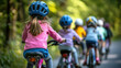 © Katerina Bond - A group of children riding bicycles on a scenic outdoor trail, wearing colorful helmets and clothing, surrounded by lush green trees, emphasizing safety and children's adventure.