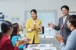 © amnaj - Asian businesspeople clapping hands during a meeting in a modern office, celebrating a successful deal or congratulating a colleague for achieving goals