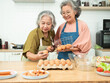 © arlee - Two Asian elderly gray haired senior woman are selecting fresh chicken eggs in egg panel at a cozy kitchen, healthy food