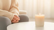 © Bonsales - Scented candle burning on a white coffee table with a woman sitting on a sofa in the background, enjoying the relaxing atmosphere