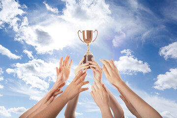 Wall Mural - woman holding golden trophy and people reaching for it against sky