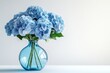 © Thimira - A bouquet of light blue hydrangeas in a teal glass vase against a white background.