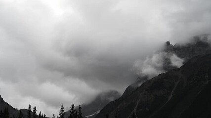 Wall Mural - Timelapse of blowing white and grey storm clouds moving between mountains above a forest
