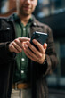 © dikushin - Vertical selective focus shot of unrecognizable man holding and using smartphone standing on city street, browsing internet, checking social media, using mobile app. Concept of modern communication.
