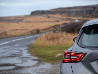 Wall Mural - A car is parked on a wet road with a view of a mountain in the background. The car is a grey. Travel to nature by car concept. Burren Ireland. Adventure with rented vehicle.