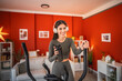 © Miljan Živković - woman hold headphones and shaker exercise on elliptical machine at home