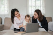 © Satori Studio - Two women and a baby bonding at home, sharing joyful moments on a sofa with a laptop.