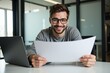 © Nina - Smiling Young Caucasian Male in Glasses Reviewing Documents at Modern Office Desk with Laptop in Bright Workspace