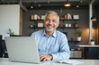© MT - Smiling Older Man Working at Laptop in Modern Office Setting with Plants and Bookshelves in Background