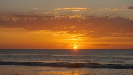 Poster - Beautiful Orange and Yellow Sunset Over the Ocean with Gentle Waves and Dramatic Clouds at Dusk