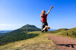 © M.studio - A joyful woman jumps in the air on a mountain trail, arms raised in excitement. The lush green landscape and blue sky create a vibrant, energetic scene