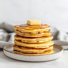 Poster - Fluffy buttermilk pancakes stacked high on a light plate with a pat of butter on top, creating a delicious breakfast delight