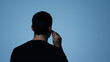 © pattozher - Whispering Secrets: An anonymous individual turns away from the viewer, hand raised to ear, perhaps listening intently or confiding a secret on a blue backdrop. This image plays on mystery, privacy.