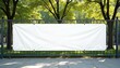 © Vadym - Long white vinyl banner on fence in urban park. Blank hoarding mockup, billboard, signage in city with green trees. Commercial advertisement, public information canvas. Mock up space.