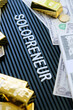 © ponsulak - Business concept. Gold bars and dollars on a black background with the word solopreneur.