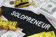 © ponsulak - Business concept. Gold bars and dollars on a black background with the word solopreneur.