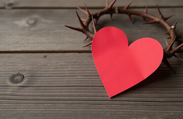 Poster - A Simple Red Paper Heart Is Placed Upon A Wooden Background Adorned With A Thorny Crown.