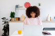© Xavier Lorenzo - Young happy African American woman using laptop sitting at kitchen table. Working from home and business concept