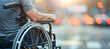 © Aleena - Close-up of an adult man in a wheelchair with his hand on the wheels and holding it, blurred background, bokeh effect, blurred city street background, concept for editorial compositions