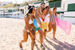 © Xavier Lorenzo - Group of cheerful young friends walking together on the beach, carrying beach toys and laughing, enjoying their summer vacation. Friendship and holiday lifestyle concept