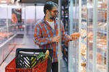Elderly man with a basket of groceries buys sausage in supermarket