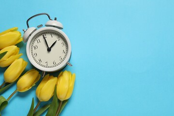 Poster - Spring time. Alarm clock and beautiful tulips on light blue background, flat lay. Space for text