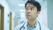 © URRMInc - A close-up of an Asian doctor with a stethoscope, looking thoughtful in a hospital corridor.