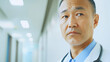 © URRMInc - A close-up of an Asian doctor with a stethoscope, looking thoughtful in a hospital corridor.