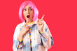 © Pixel-Shot - Shocked young woman in wig pointing at something on red background. Accusation concept