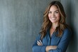 © Alice Y - A confident woman smiles warmly against a textured gray wall, her long, wavy hair framing her face. She wears a stylish blue blouse, embodying positivity and professionalism.