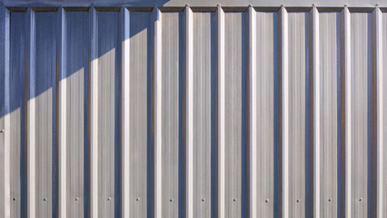 Gray corrugated metal exterior wall background of warehouse building or cargo container with light and shadow on surface