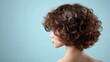 © O - Back view of young caucasian woman with short curly brown hair against blue background