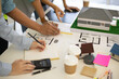 © Kield KD - A person is drawing a house on a table with a calculator and a ruler. The person is wearing a yellow vest