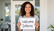 © Margarita - Smiling woman holding welcome interns sign in an office for blogs, websites, internship promotions, recruitment materials, human resources presentations, and professional networking