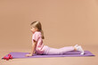 © New Africa - Cute little girl exercising on fitness mat against dark beige background