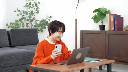 Leinwandbilder - リビングルームでスマホとノートパソコンを使うミドル女性